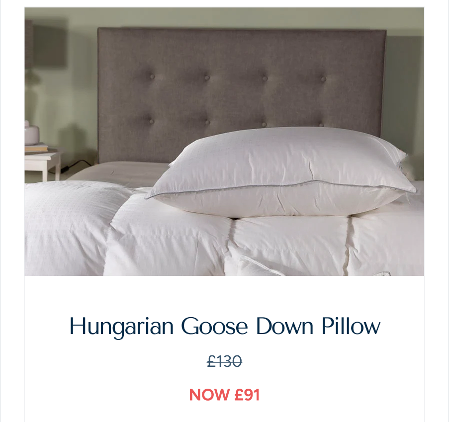 A lifestyle shot of a "Hungarian Goose Down Pillow" resting on a white duvet with a grey padded headboard in the background, labeled: "Hungarian Goose Down Pillow, reduced price after discount"